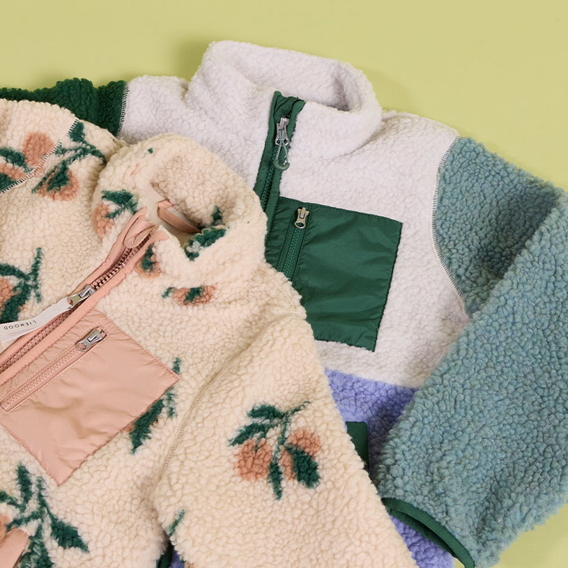 Barn i fleecetröja sitter utomhus i naturmiljö.