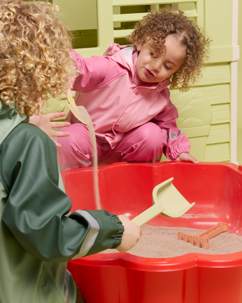 Två barn leker i en röd sandlåda, med texten 'Utelek Sandlådor'.