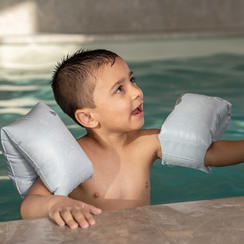 Pojke med puffar i poolen, tittar uppåt.