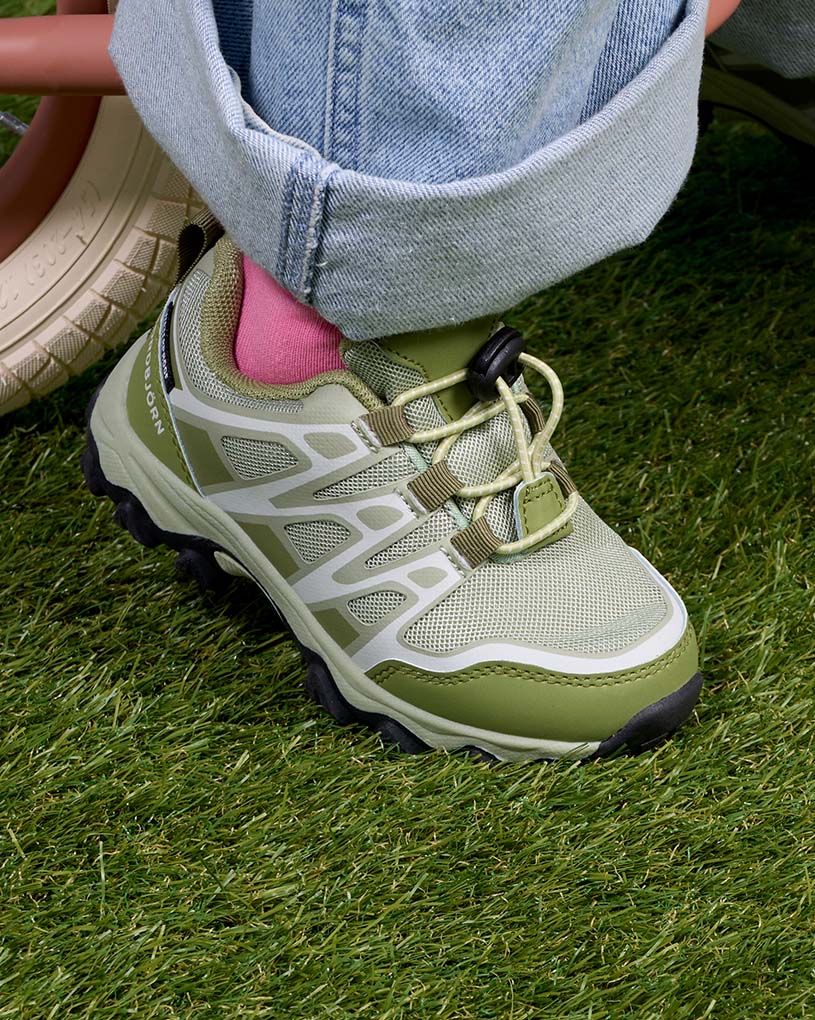 Gröna barnskor med kardborreband och vita detaljer på fötter i vita strumpor.