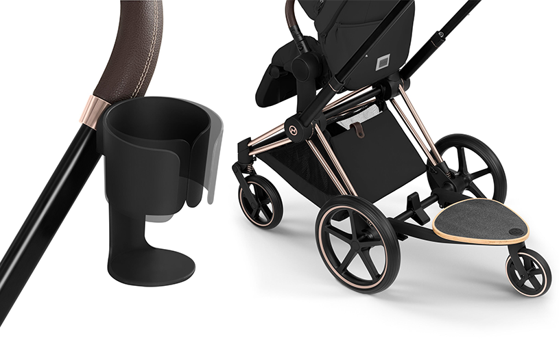 Svart Cybex barnvagn med roséguldsdetaljer, mugghållare och ståbräda. Brun läderhandtag visas i närbild.