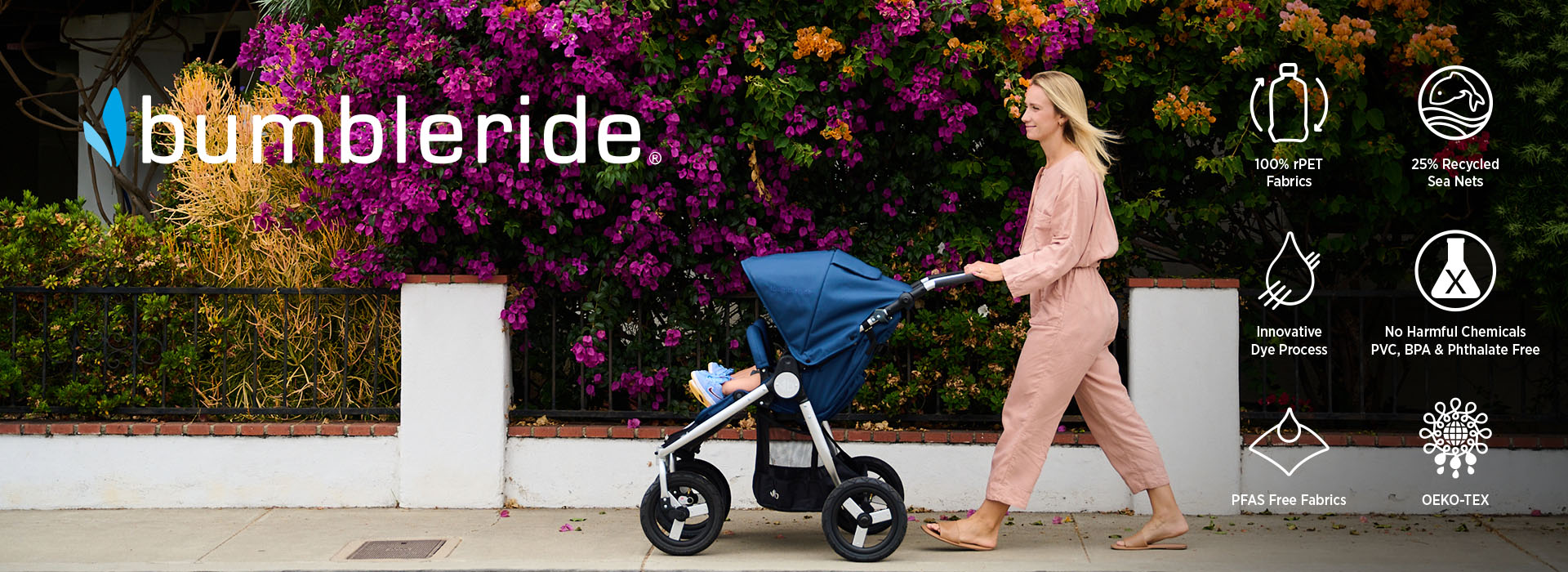 Kvinna går med barnvagn framför färgglad buske.