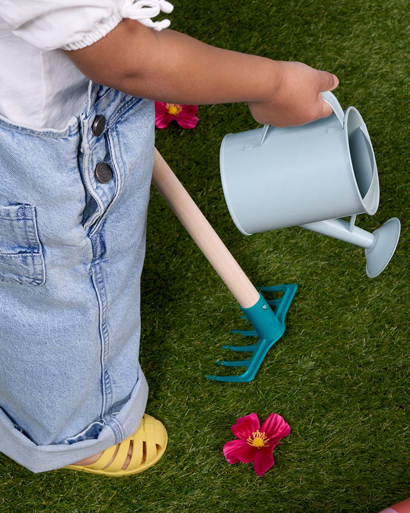 Barn häller vatten i blå sandlåda utomhus.
