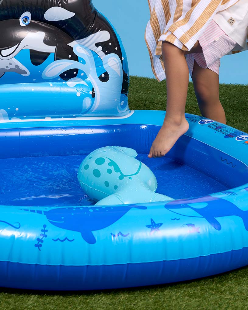 Flicka med flytring i en blåvit pool utomhus.