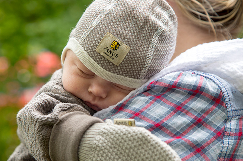 Bebis sover i en vuxens famn utomhus.