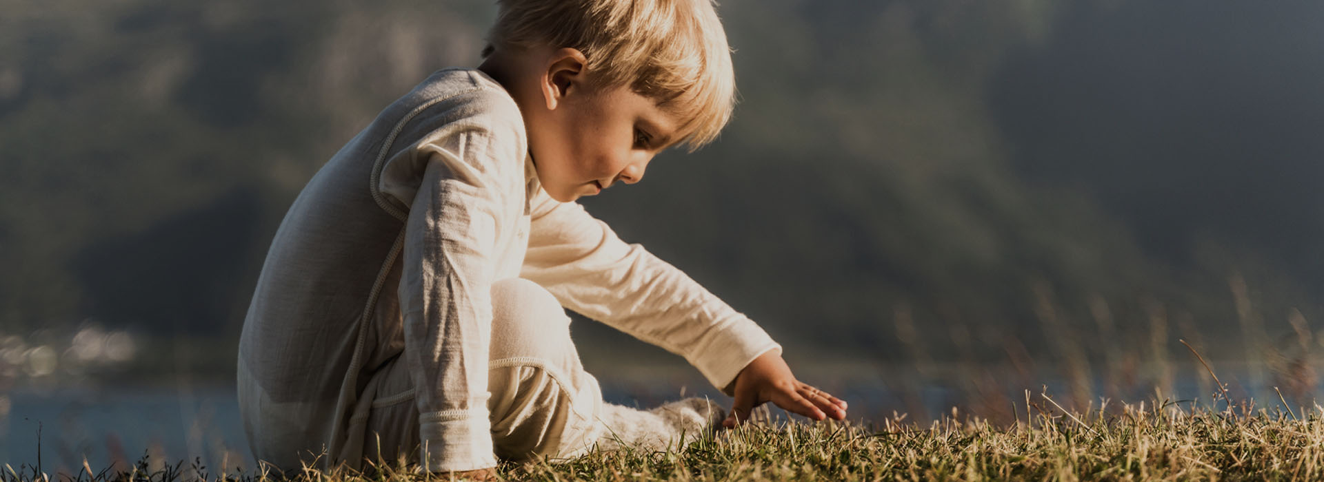 Liten pojke i vit pyjamas leker på en gräsmatta i naturen.