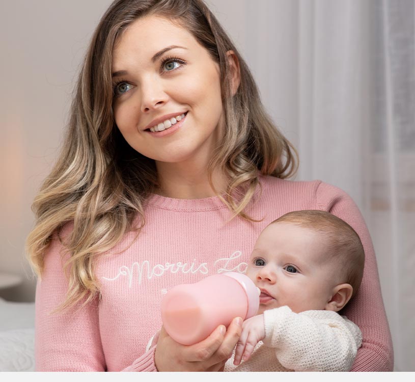 Kvinna i rosa tröja matar bebis med rosa flaska.