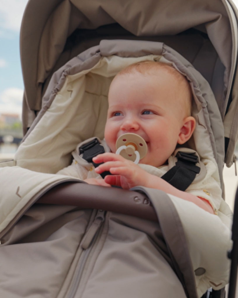 Bebis i barnvagn med napp i munnen, mot blå himmel.