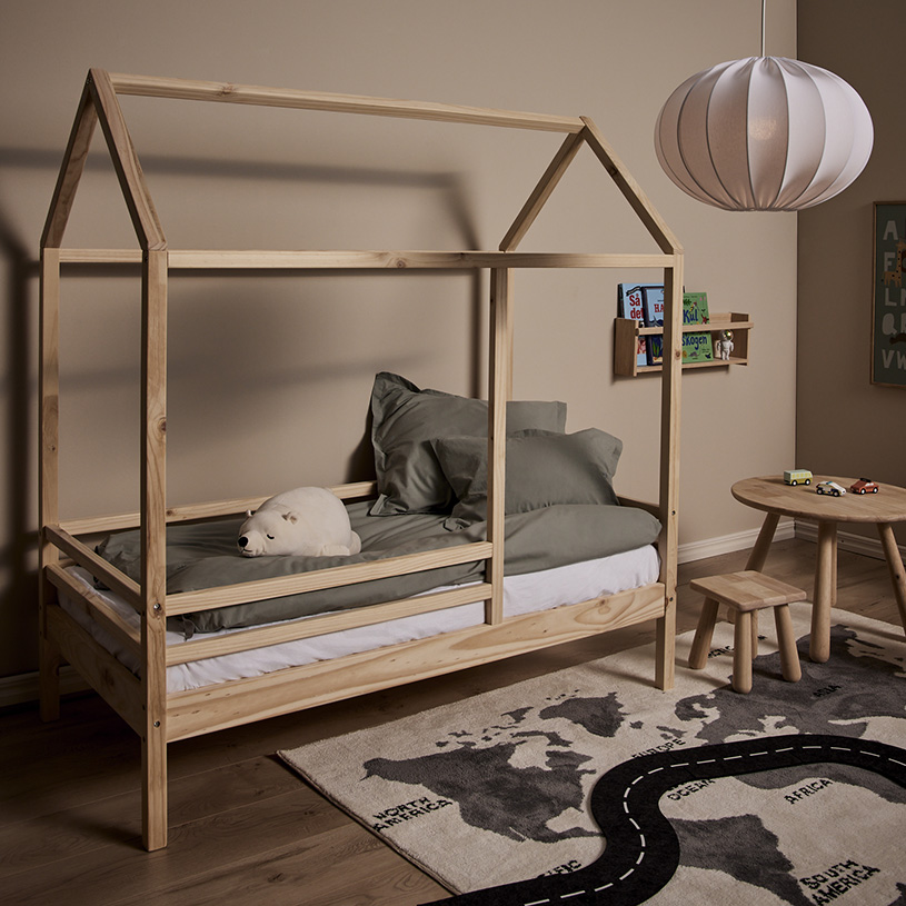 Barnsäng i trä med husformad ram, nallebjörn, lampan över bord och leksaker.