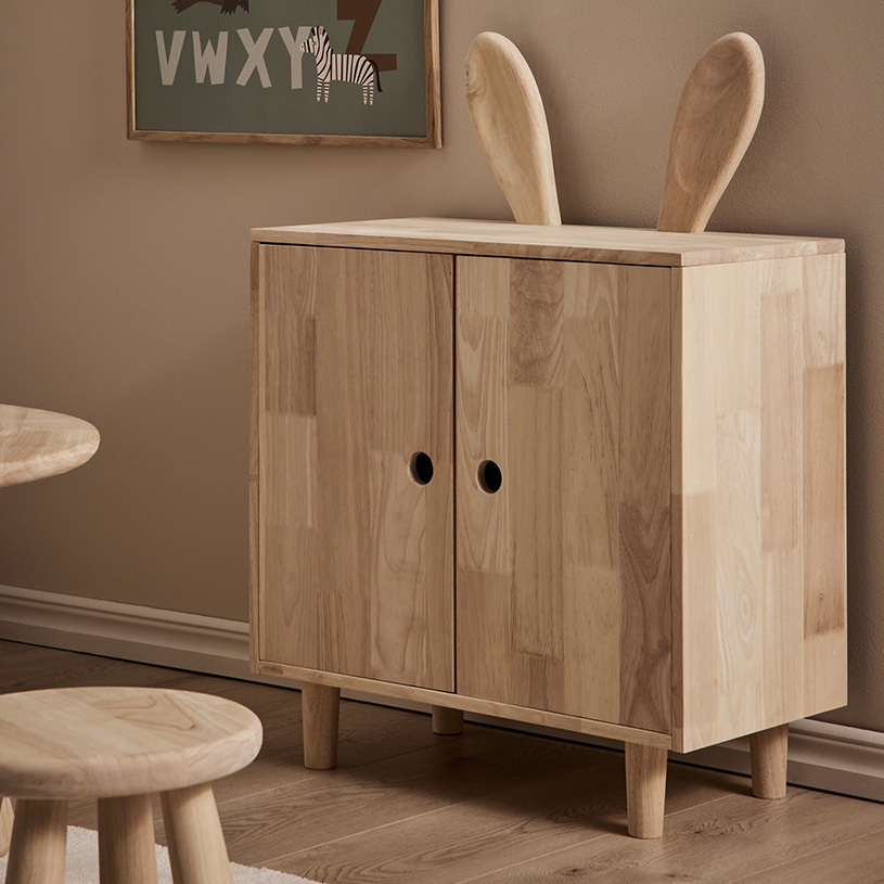 Träskåp med kaninöron på toppen, står mot en beige vägg.