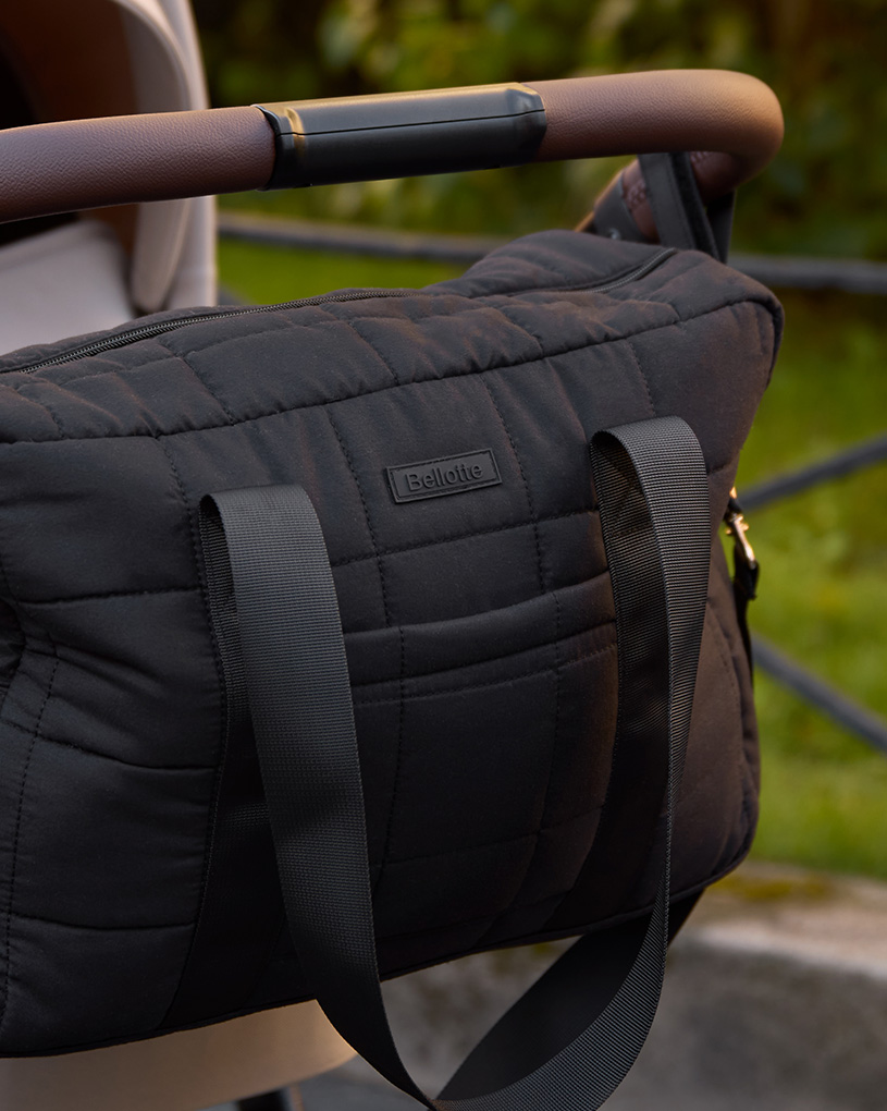 Svart quiltad skötväska hängande på barnvagnshandtag utomhus.