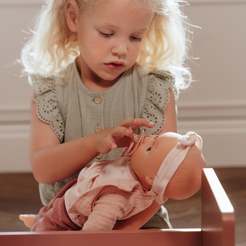 Liten flicka leker med en docka i en trähylla.