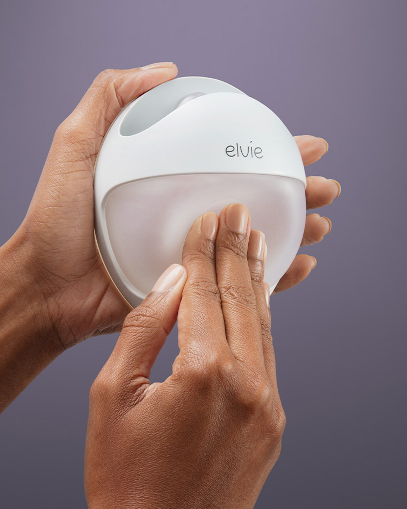 Händer håller en vit Elvie-bröstmjölksuppsamlare mot lila bakgrund.