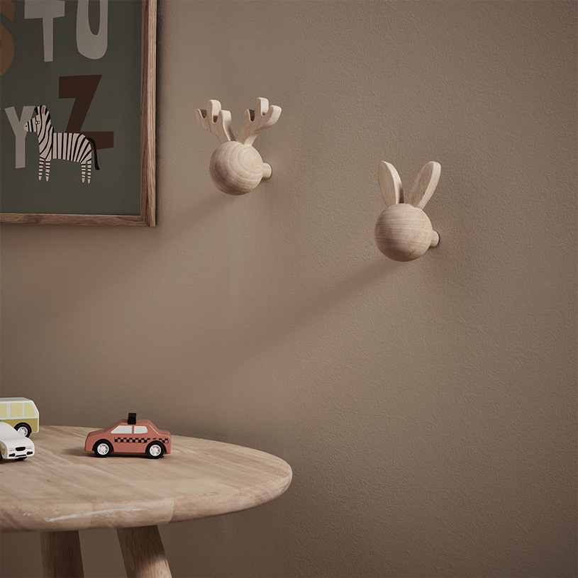 Vägghängare i trä med horn och öron bredvid leksaksbilar på ett bord.