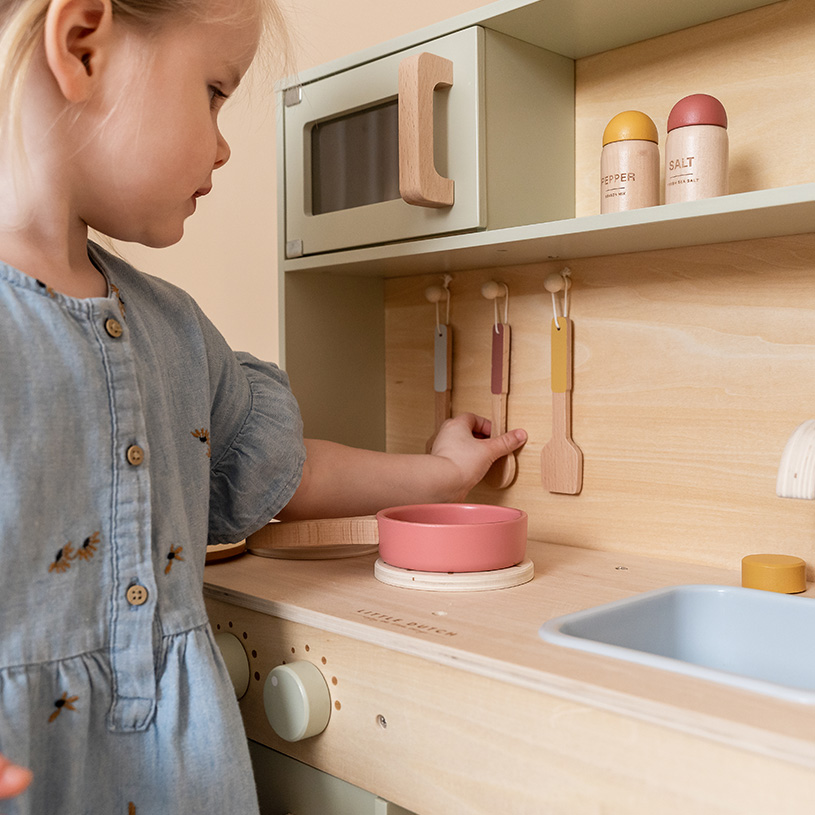 Flicka leker med leksakskök, rör vid träskedar och kryddburkar.
