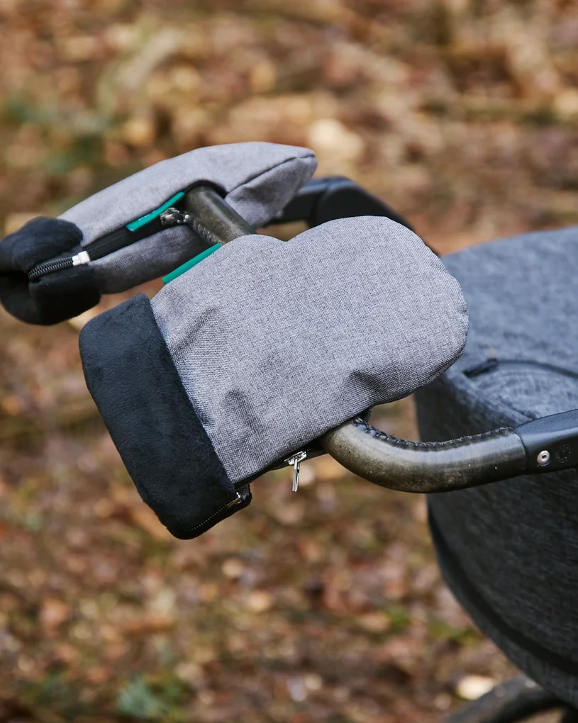 Händer i vantar greppar ett barnvagnshandtag på en träbrygga.