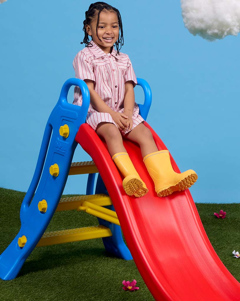 Barn med rosa hatt åker rutschkana utomhus.