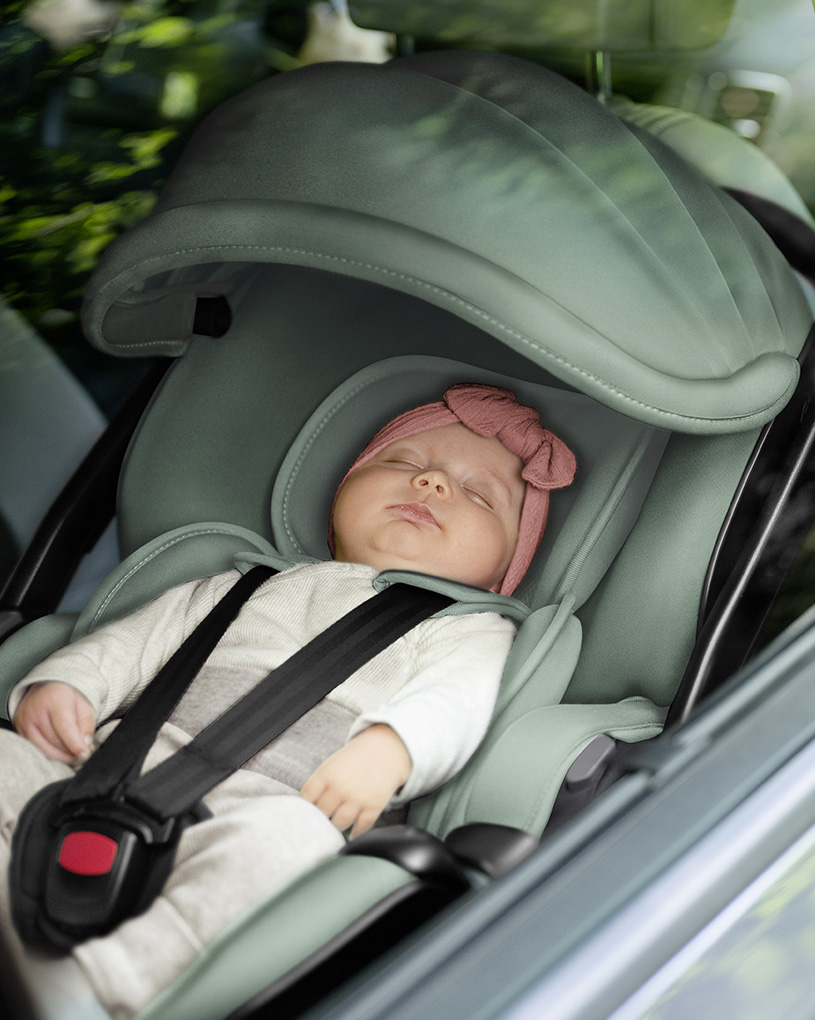 Baby sover i bilbarnstol inuti en bil.