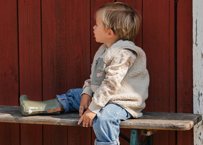 Barn sitter på en bänk iförd väst och gummistövlar, med texten 'Kenza X Viking'.