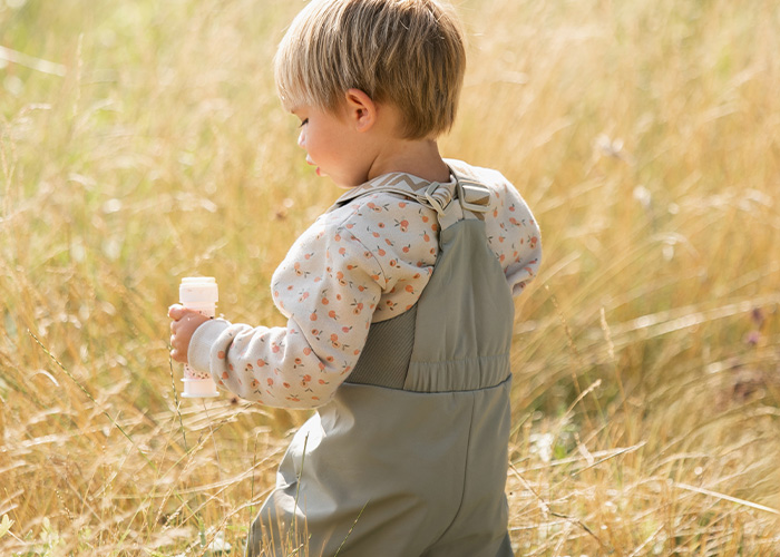 Barn i grå overall håller en flaska, med texten 'Kenza X Viking'.