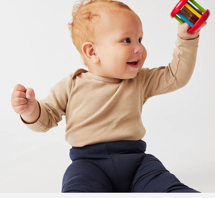 Bebis i beige tröja leker med färgglad leksak.