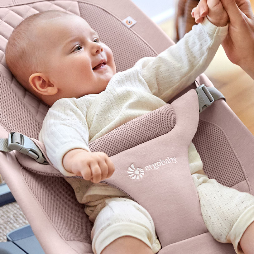 Bebis i en grå babysitter med leende ansikte.