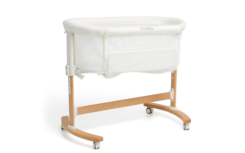 Vit spjälsäng med träram och hjul mot ljus bakgrund.