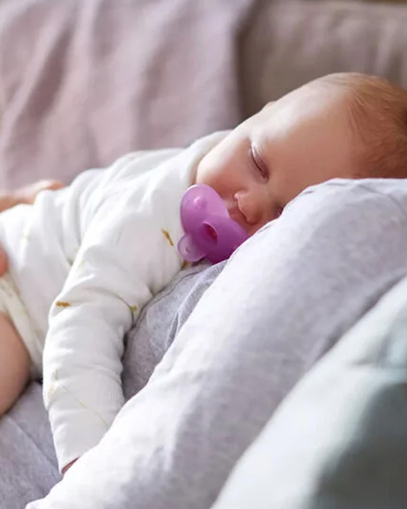 Bebis sover med napp i munnen på en vuxens bröst.