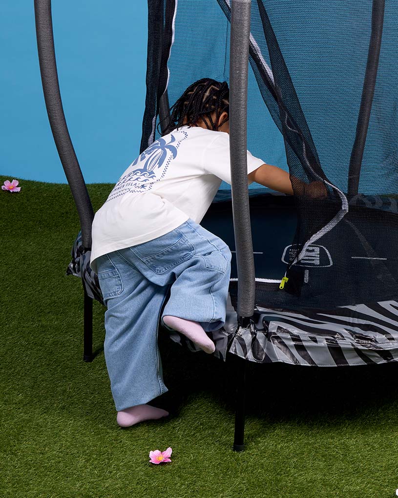 Två barn sitter på en filt med fika i en trädgård.