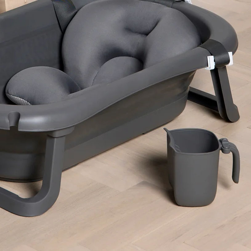 Vit och grå babybadbalja med dyna, står på trägolv.