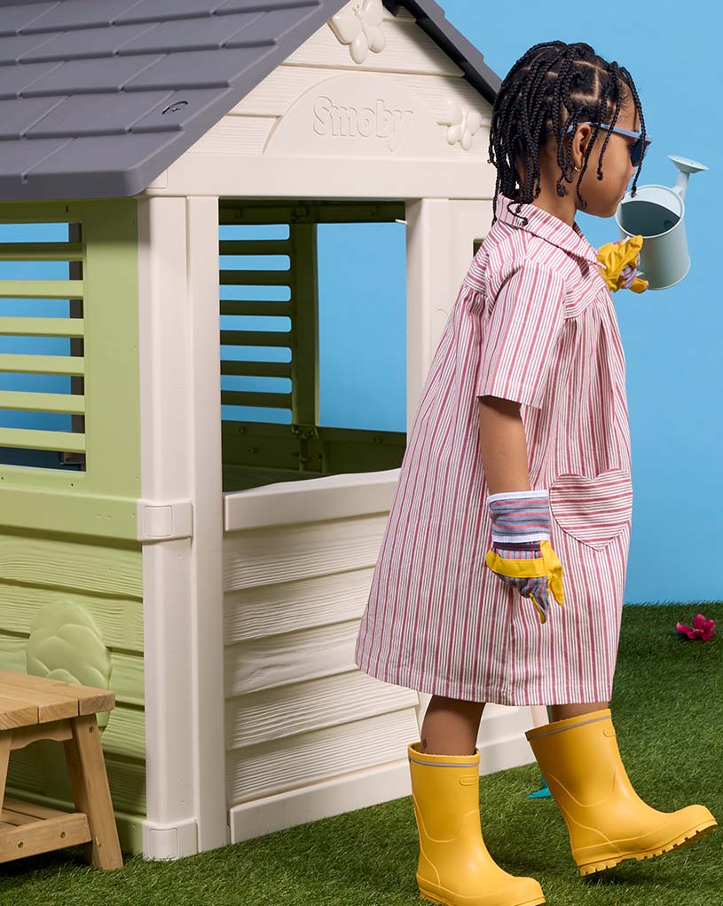 Barn i grön jacka kikar in genom fönstret på vit byggnad.