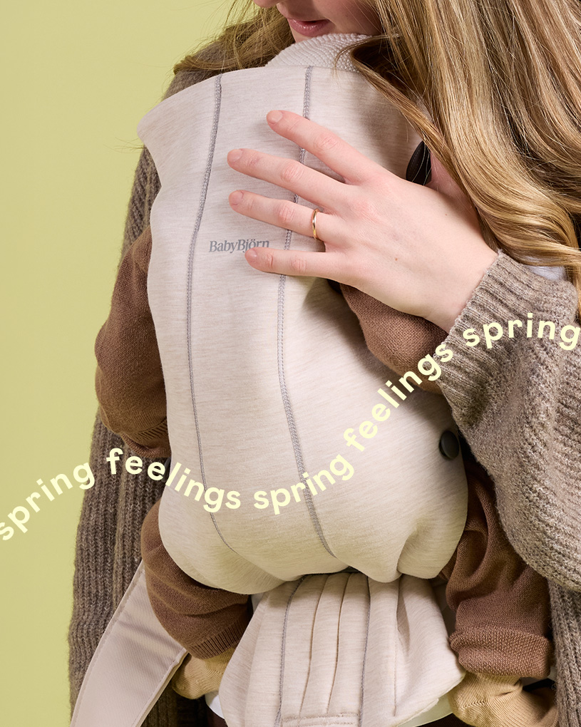 Kvinna håller baby i bärsele med texten 'spring feelings spring feelings'.