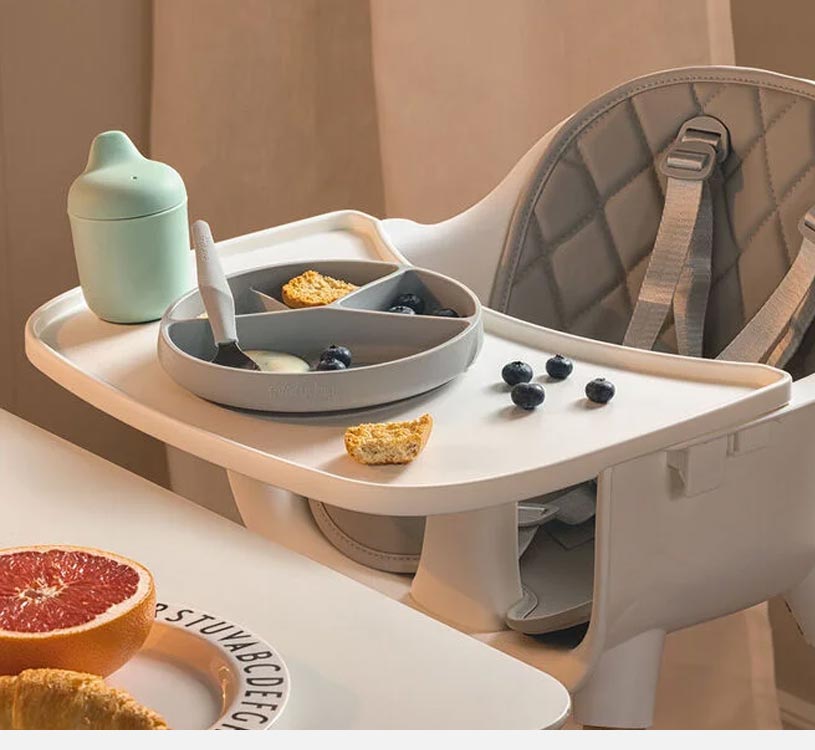 Barnstol med bricka, tallrik med mat, bär och pipmugg.