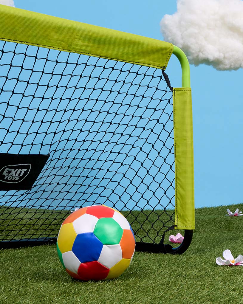 Barn i keps spelar med boll utomhus.