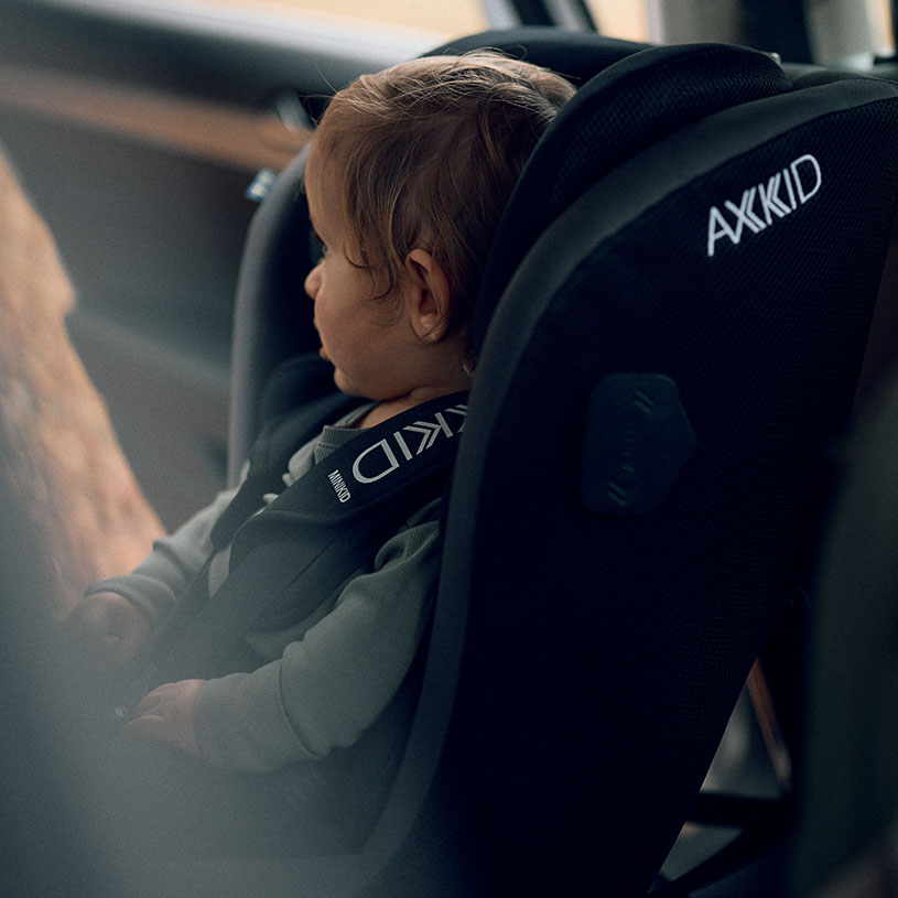 Två små barn i bilbarnstolar, ett skrattar och ett ser ut genom fönstret.