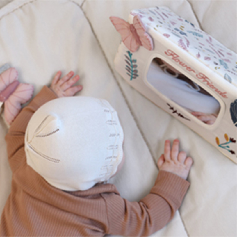 Bebis ligger på mage bredvid låda med fjärilar.