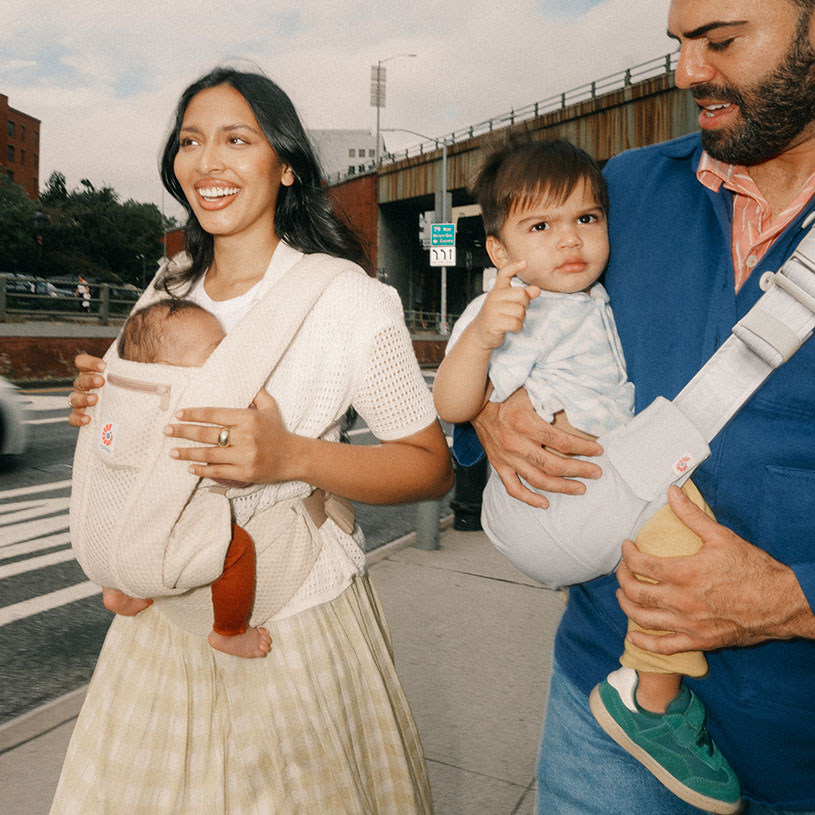 Kvinna bär en bebis i sele vid solnedgång.