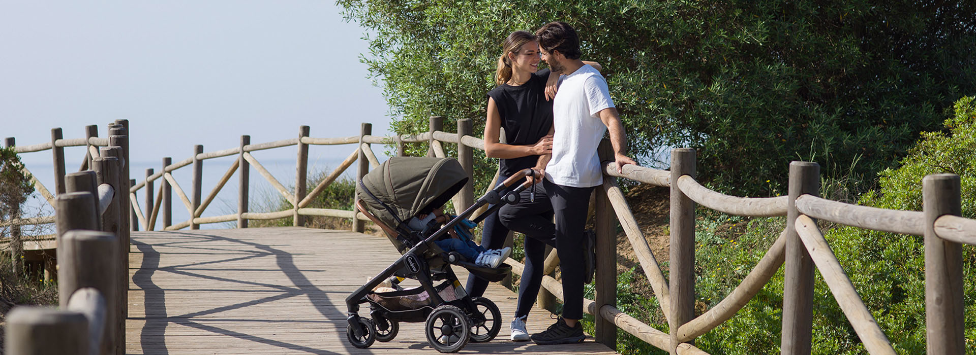 Par med barnvagn på träpromenad vid havet.