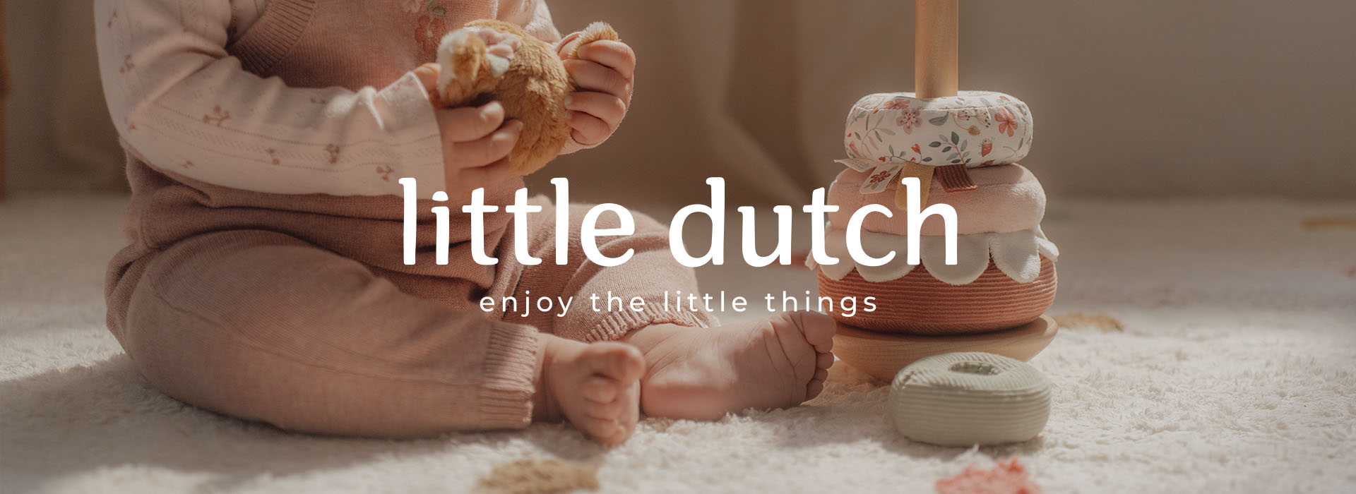 Baby leker med nalle och leksaksringar på en matta.