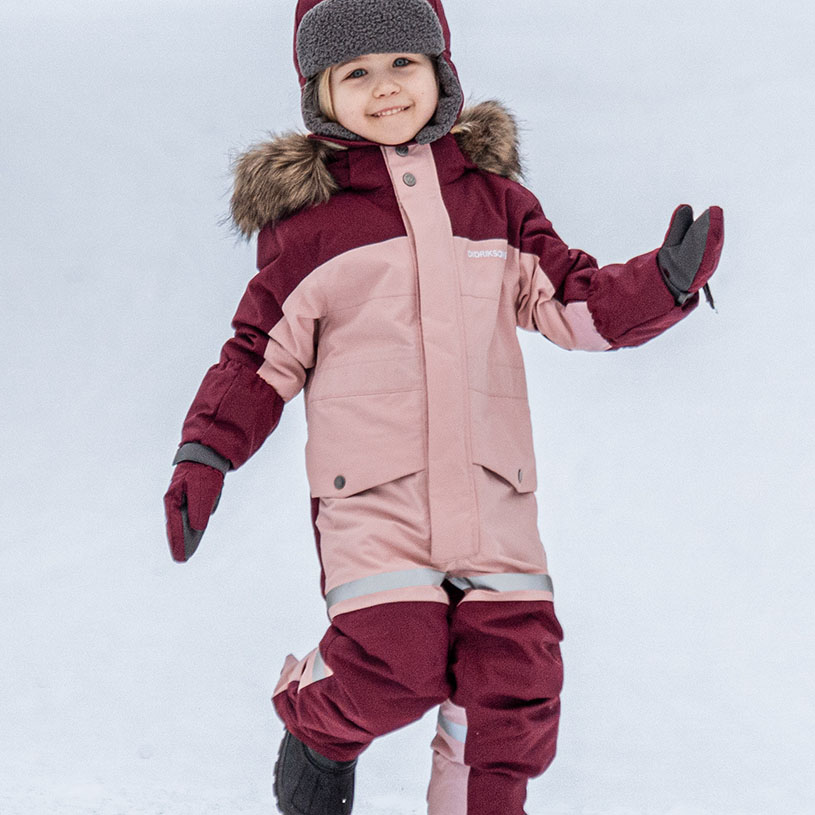 Barn i vinteroverall och mössa leker i snön.