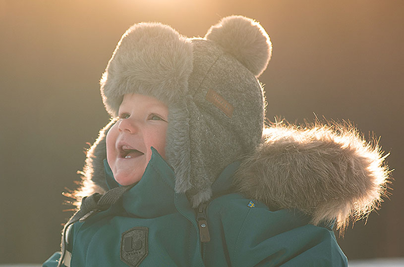 Leende barn i tjock vintermössa med solnedgång i bakgrunden.