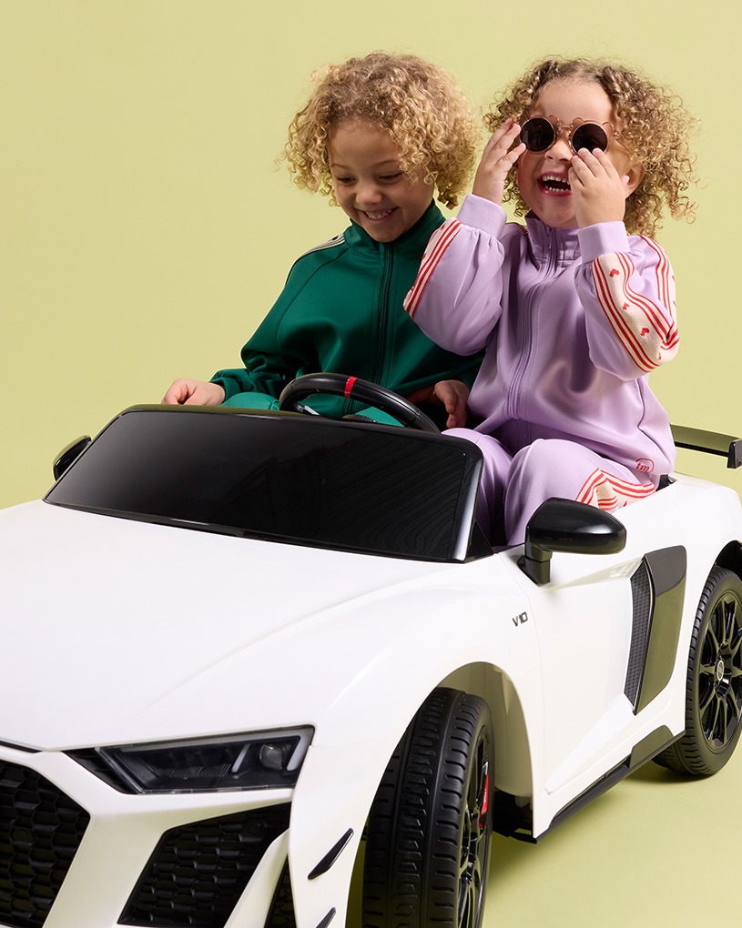 Två glada barn i en vit elbil med texten 'Utelek Elbilar'.