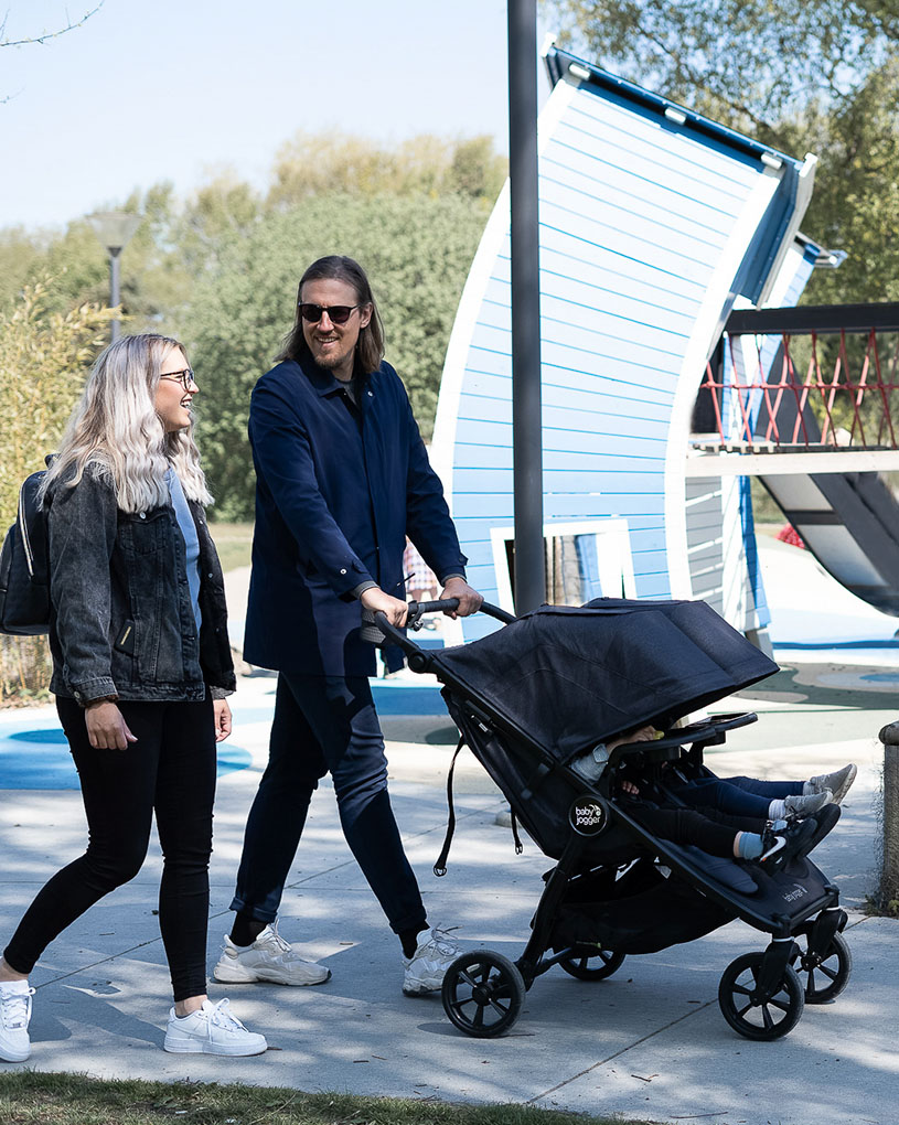 Man och kvinna promenerar med en barnvagn utomhus.