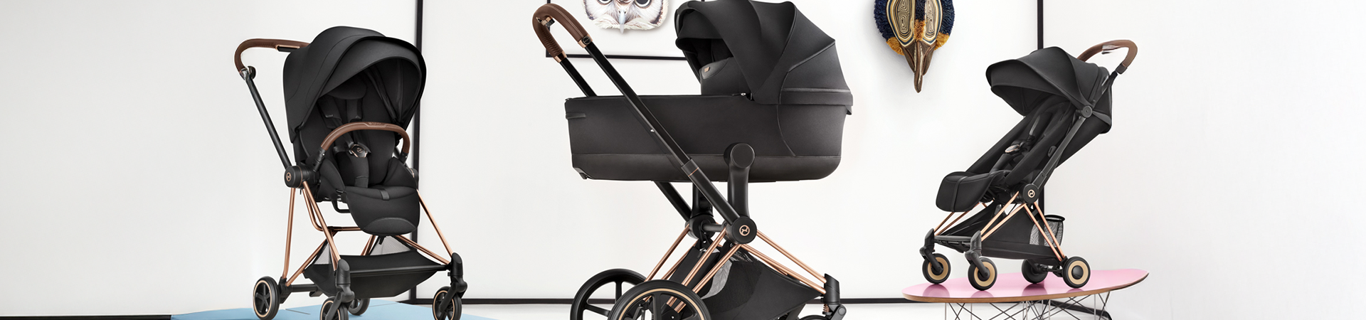 Tre svarta Cybex-barnvagnar med eleganta chassin i roséguld och bruna detaljer mot en vit bakgrund.