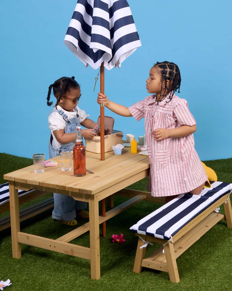 Barn i solglasögon och leopardpyjamas på bänk med kudde.