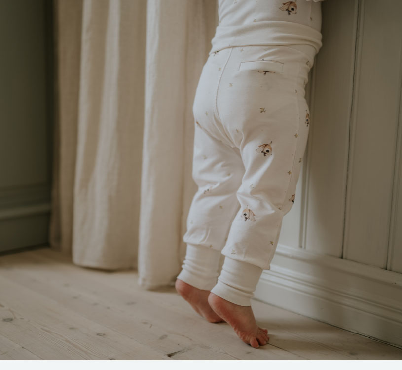 Barn i vita pyjamasar står på tå framför gardin.