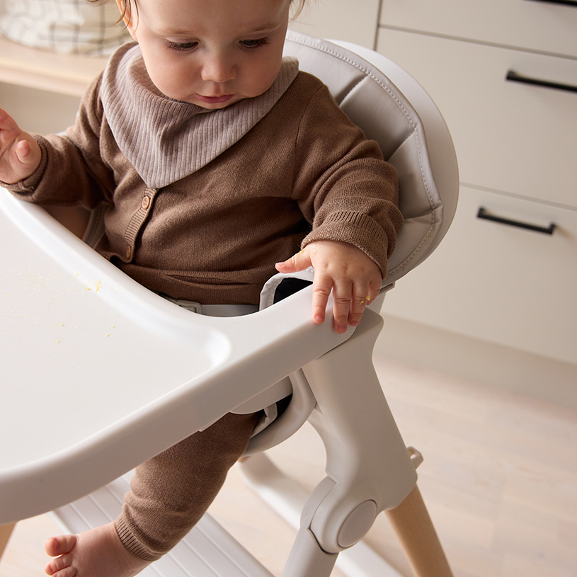 Bebis i barnstol med tallrik och mugg på bordet.