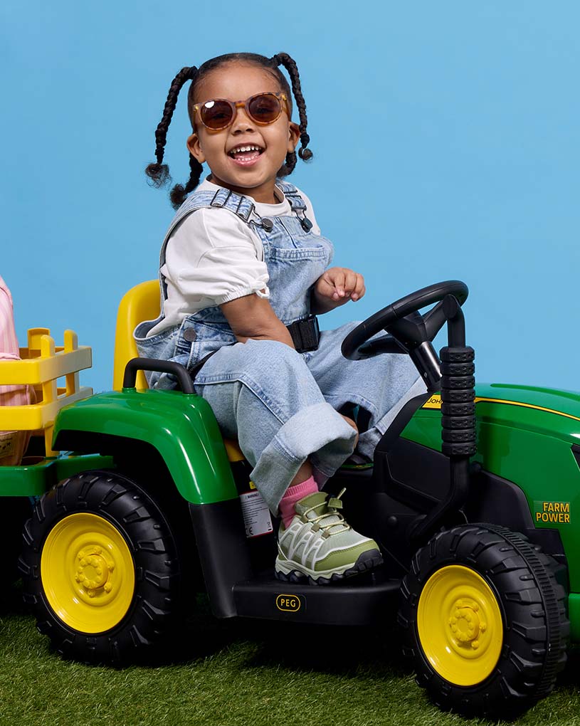 Barn i grön jacka och hatt kör svart leksaksbil.