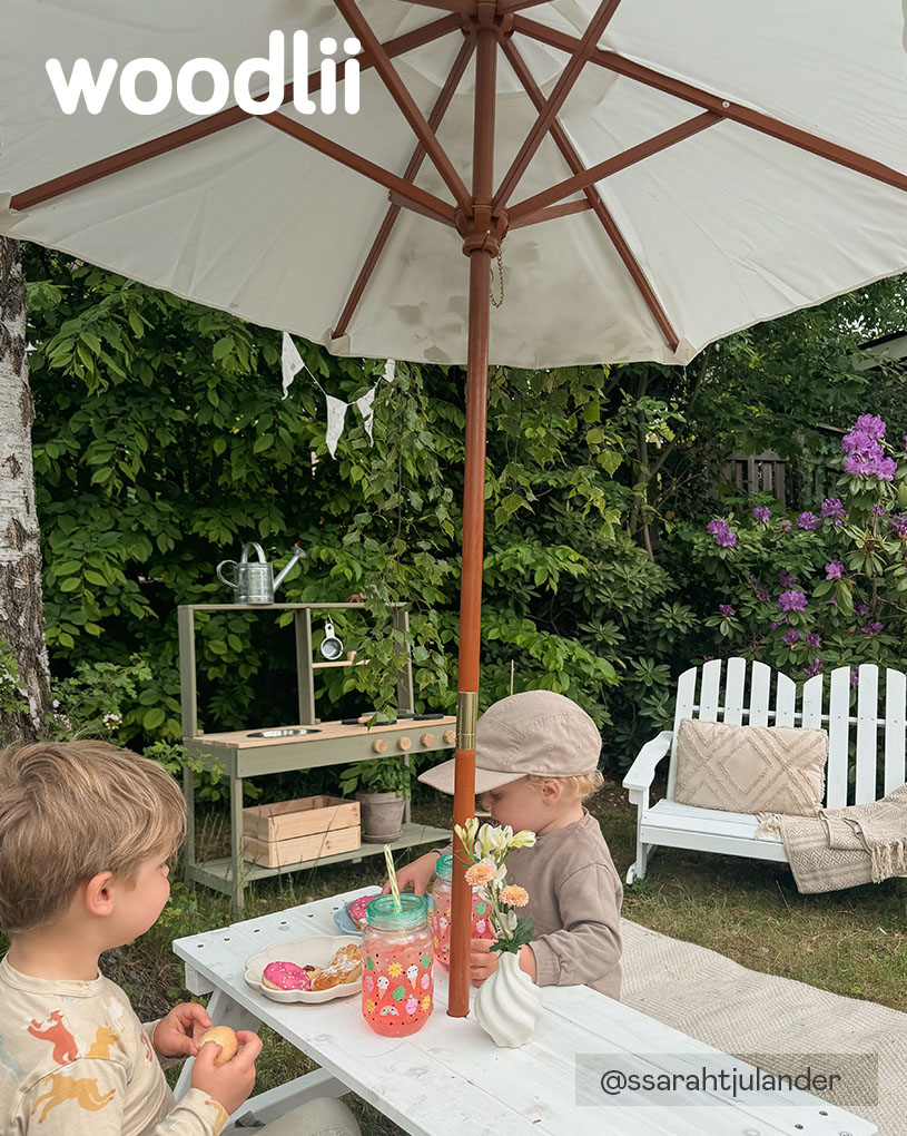 Två barn sitter vid ett bord under ett parasoll med texten 'woodlii'.