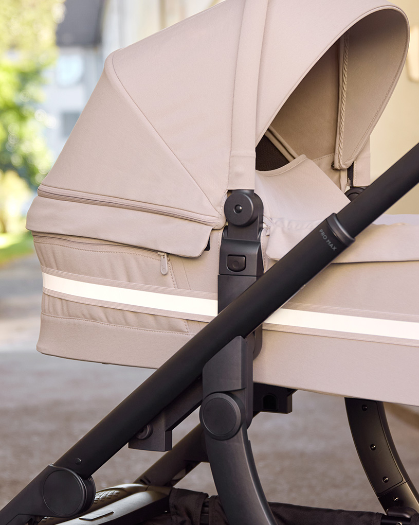 Svart barnvagn med ljus reflektor på huvan mot mörk bakgrund.